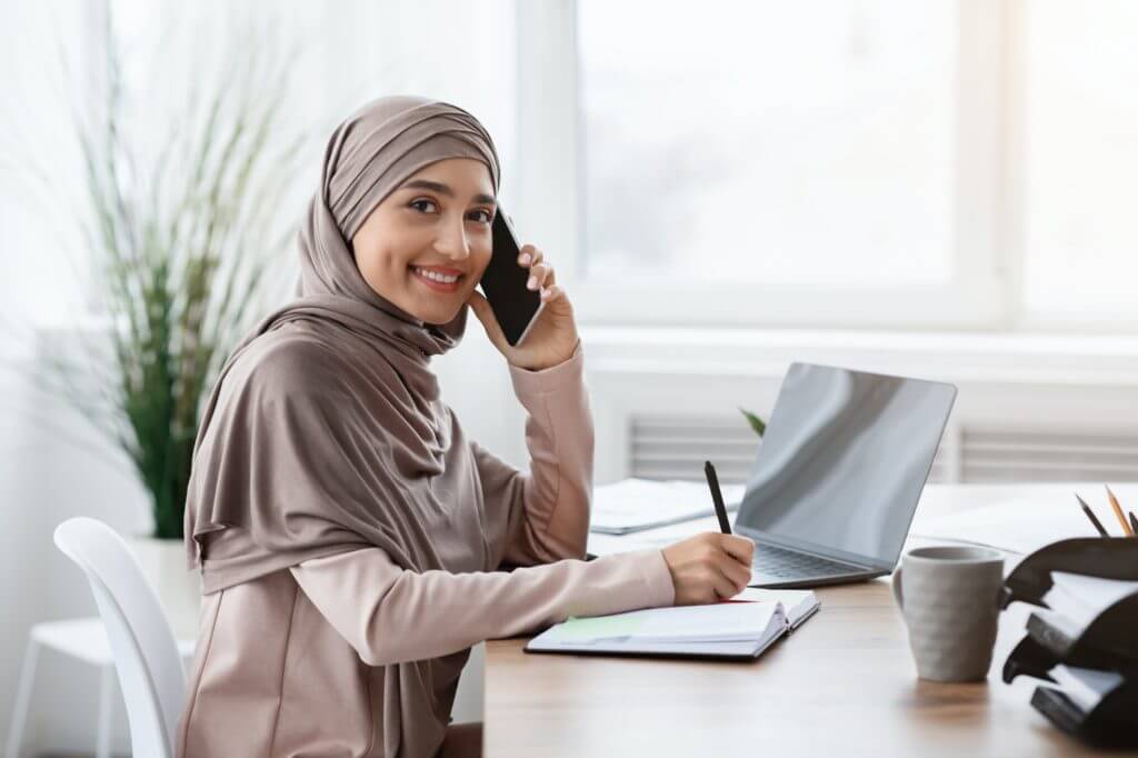 Arabic Female Secretary Talking On Cellphone And Taking Notes In Office