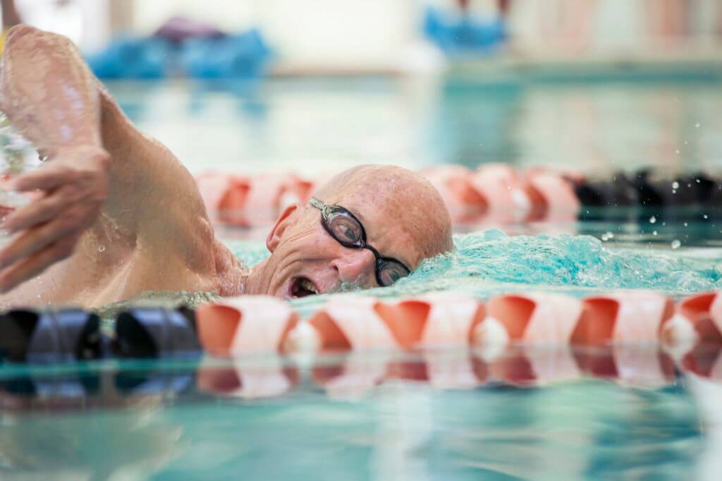 Close up shot of man in his mid 70s swimming laps in a pool.