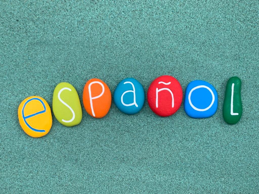 Español word composed with multi colored stone letters over green sand