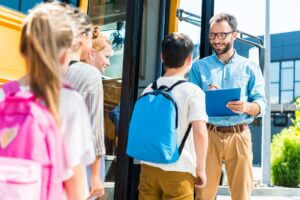 pupils entering school bus while teacher writing in clipboard