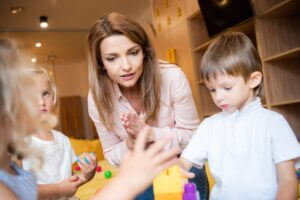 selective focus of educator and kids playing with educational constructor in kindergarten