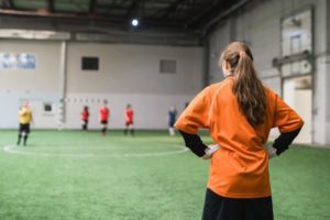 Back view of young female goalkeeper in sports uniform standing on field