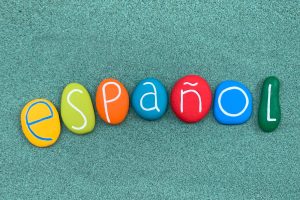 Español word composed with multi colored stone letters over green sand