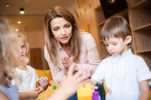 selective focus of educator and kids playing with educational constructor in kindergarten
